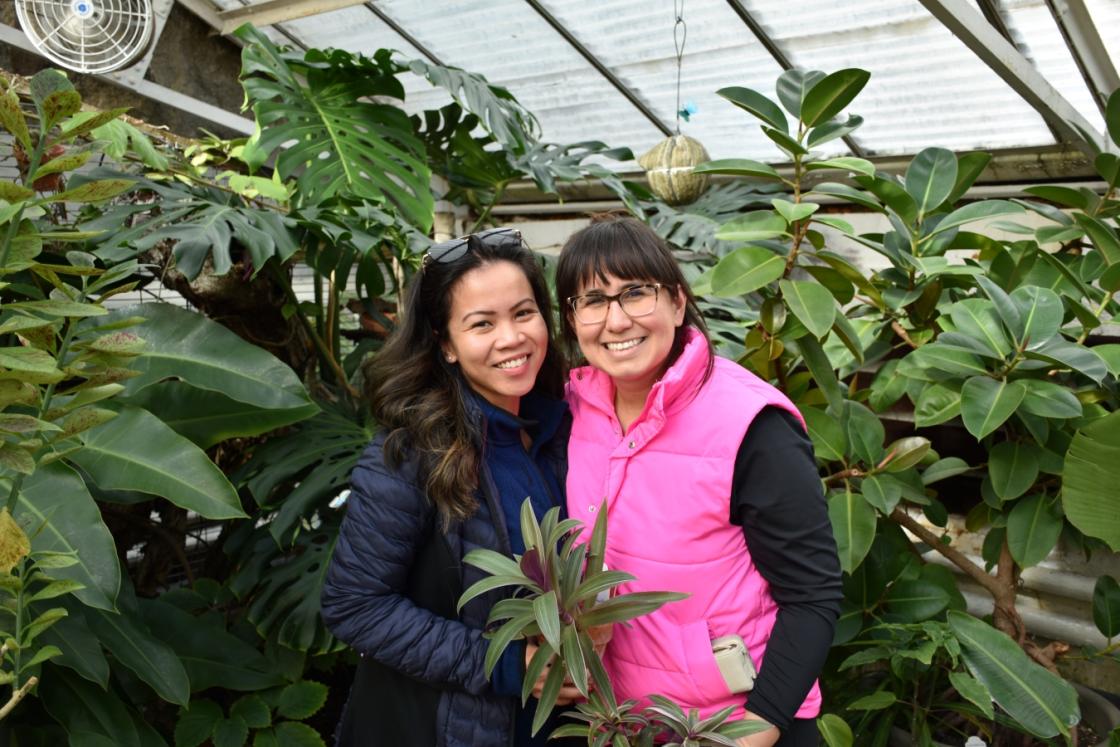 Photo of two visitors smiling and holding houseplants in the Greenhouse at Cranbrook House & Gardens.